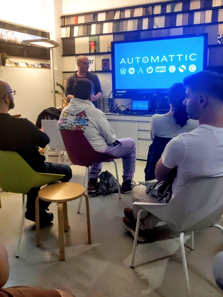 Man talking to a small audience with a screen in the background.